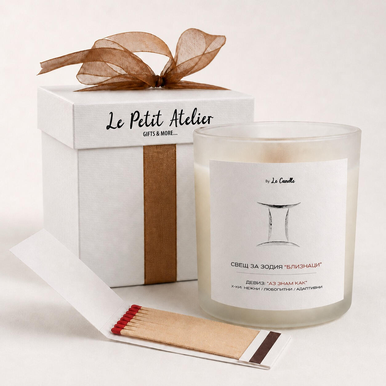 Подаръчен комплект Le Petit Atelier с ароматна соева свещ за зодия Близнаци, бронзова панделка, кибритена книжка и бяла кутия.