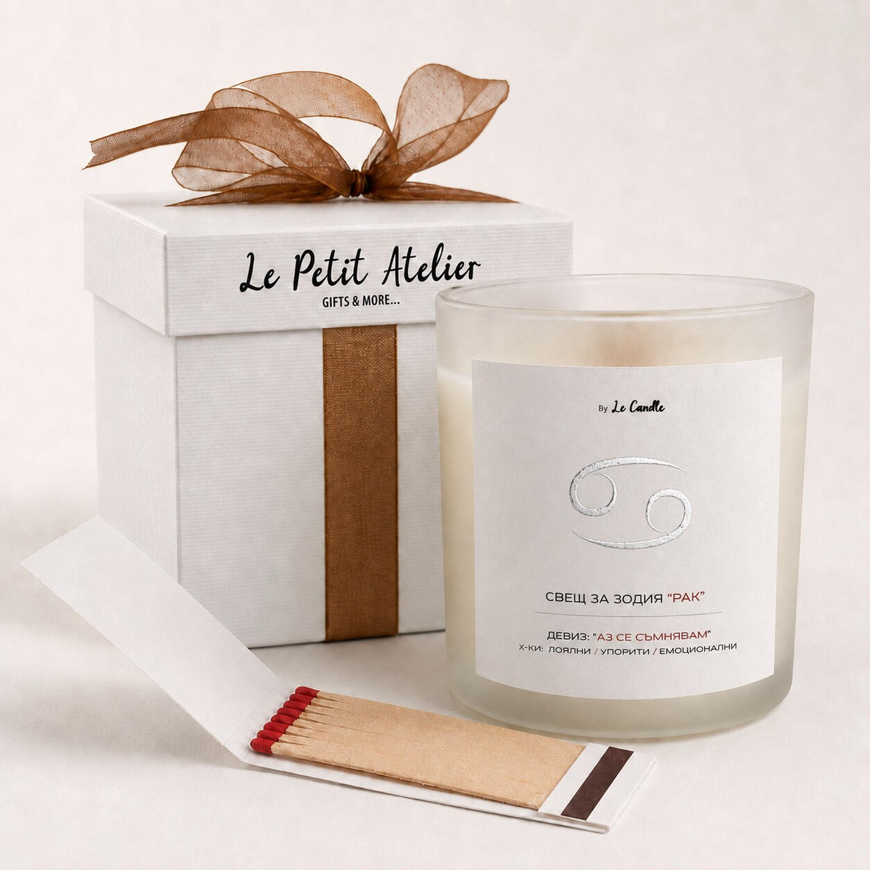 Детайлен кадър на подаръчен комплект Le Petit Atelier със свещ за зодия Рак, бронзова панделка и кибритена книжка.