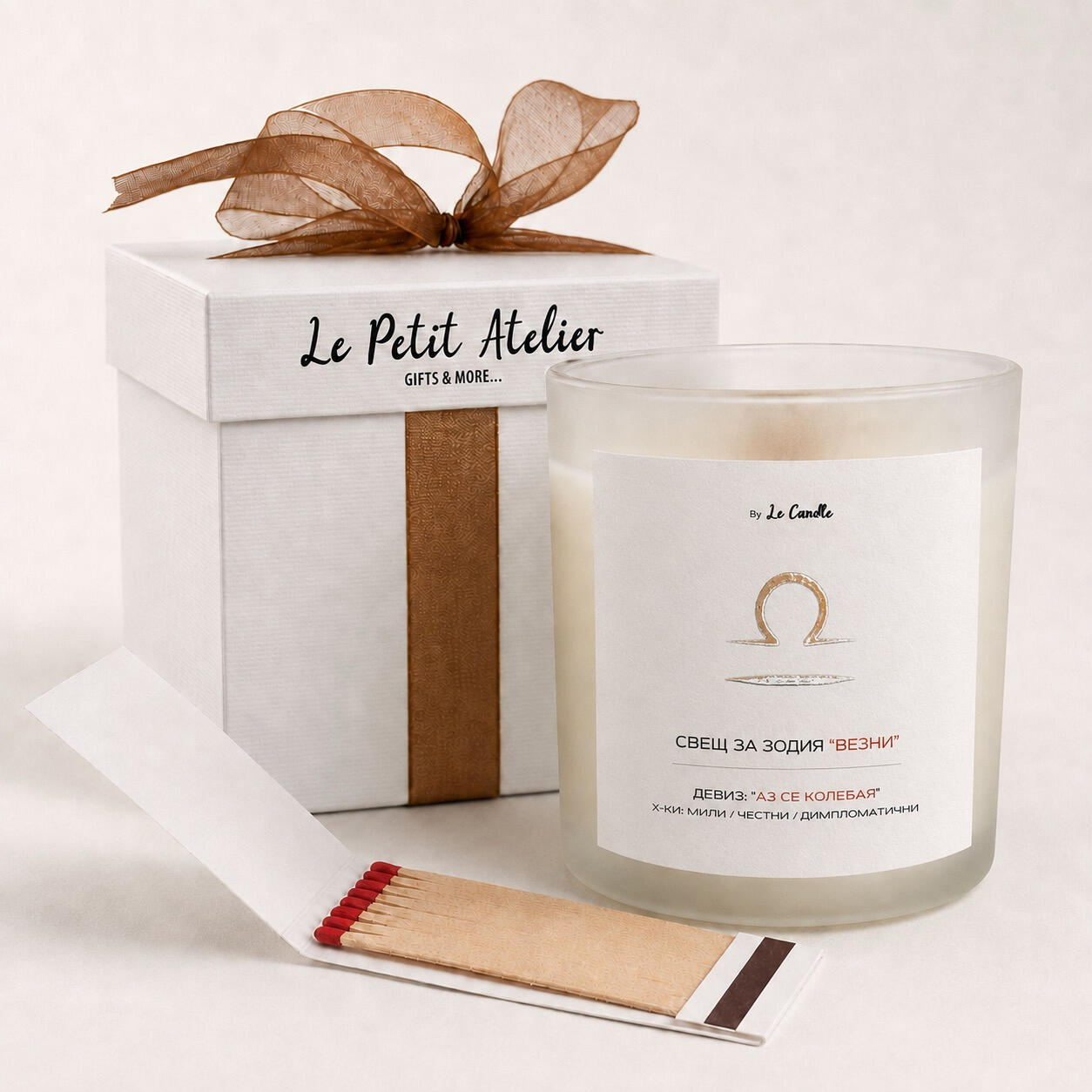 Подаръчен комплект Le Petit Atelier с ароматна соева свещ за зодия Везни, бронзова панделка, кибритена книжка и бяла кутия.