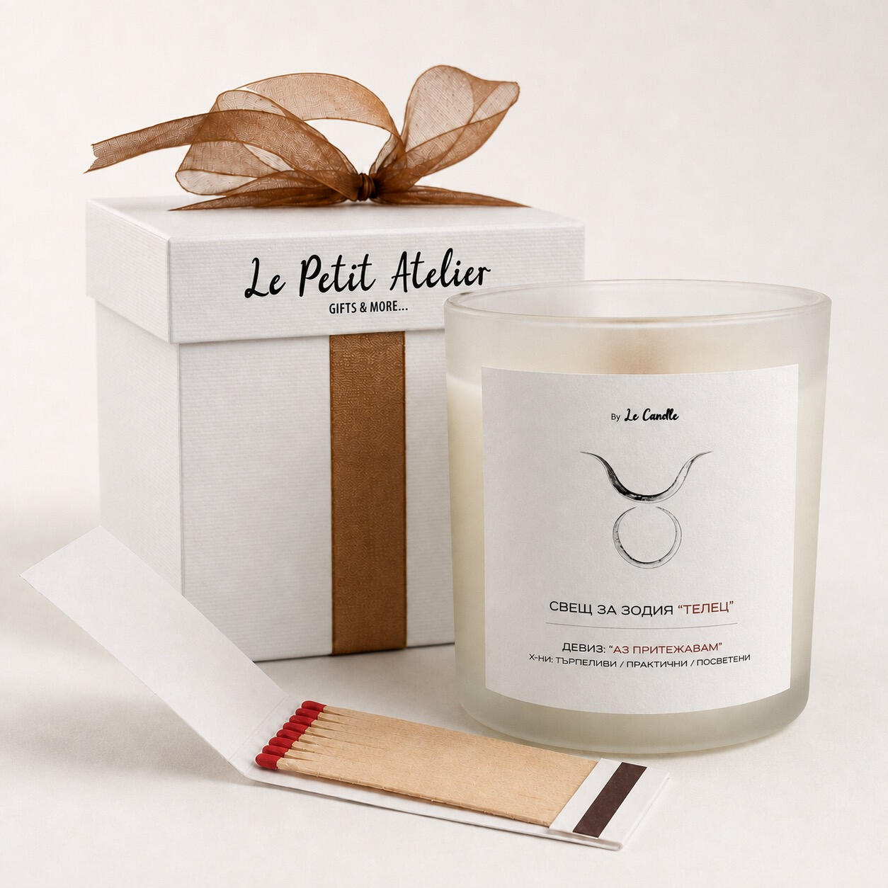 Детайлен кадър на подаръчен комплект Le Petit Atelier със свещ за зодия Телец, бронзова панделка и кибритена книжка.